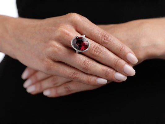 Hand wearing an oval reddish purple tourmaline and diamond ring