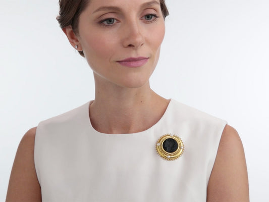 Woman wearing a gold intaglio brooch with pearl accents on a white top