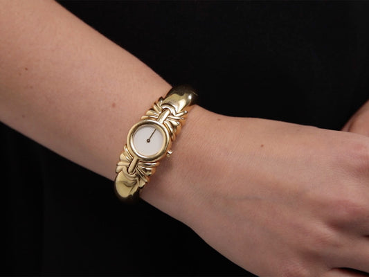 Gold watch with white dial and decorative bracelet on wrist
