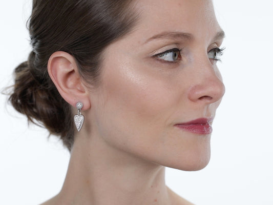 Woman wearing diamond heart drop earrings in white gold