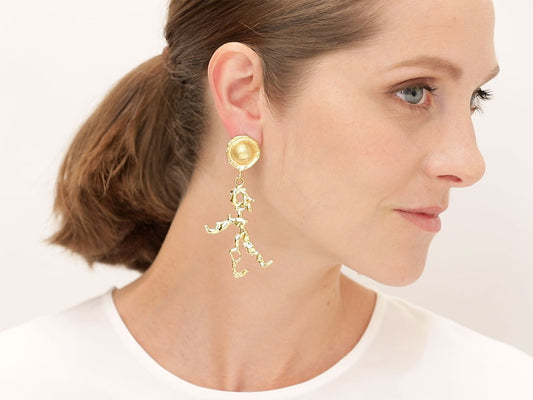 Gold drop earring with abstract figure on a woman’s ear