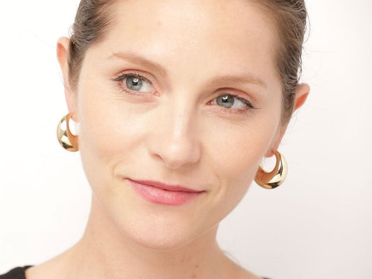 Model wearing large polished 18K gold crescent hoop earrings