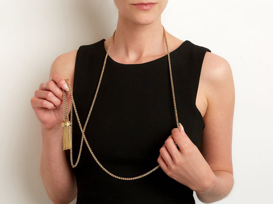 Woman wearing a long gold tassel necklace with black enamel pendant