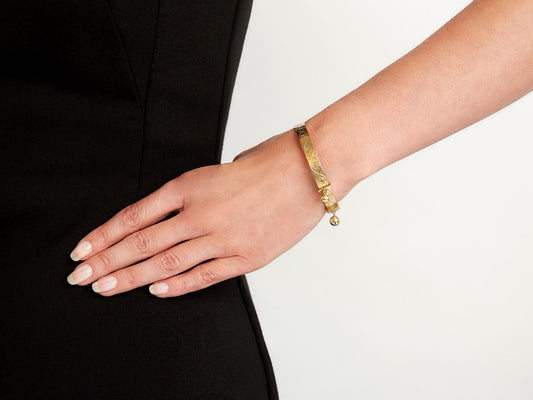 Wrist wearing a polished 18K gold bangle with hanging bells