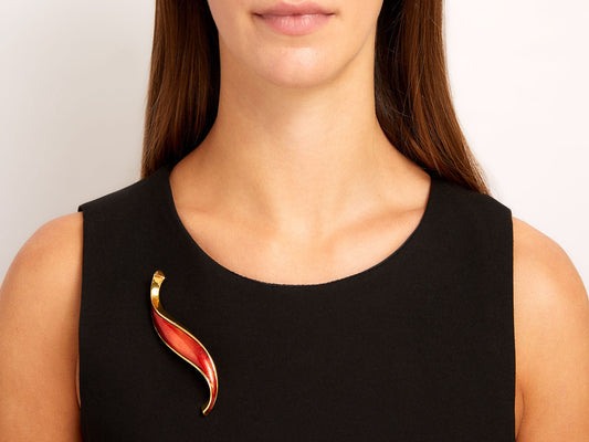 Reddish orange enamel swirl brooch in 18K yellow gold on black dress
