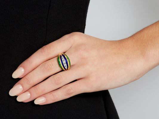 Hand wearing a gold ring with blue green enamel and diamonds