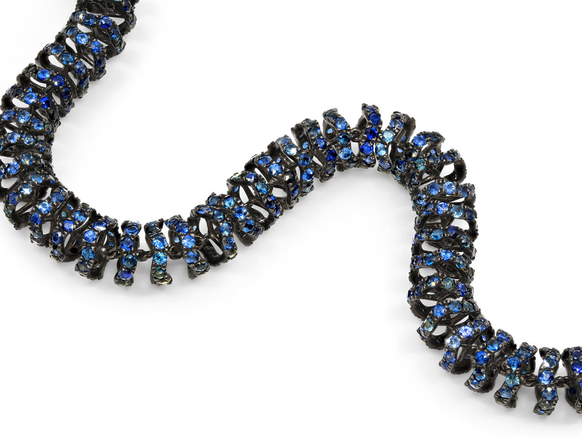 Close up of a flexible blackened gold bracelet with blue sapphires