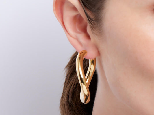 Curved 18K gold hoop earring worn on an ear