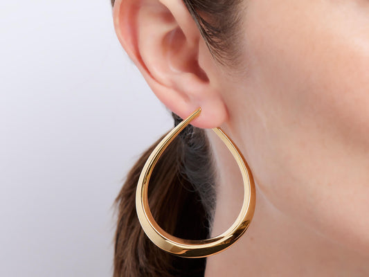 Polished 18K yellow gold teardrop earring worn on an ear