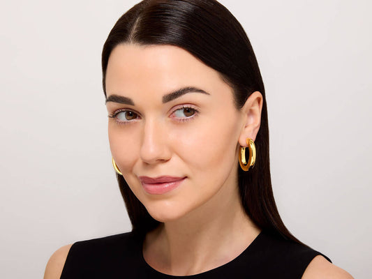 Woman wearing polished 18K gold oval hoop earrings