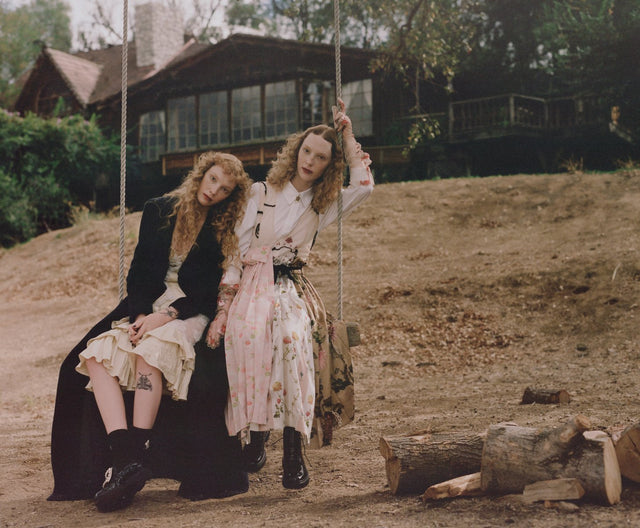 Two women sitting on a swing outdoors near a rustic cabin