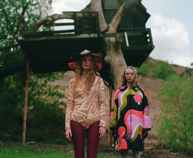 Two women in colorful outfits standing outdoors near a wooden structure