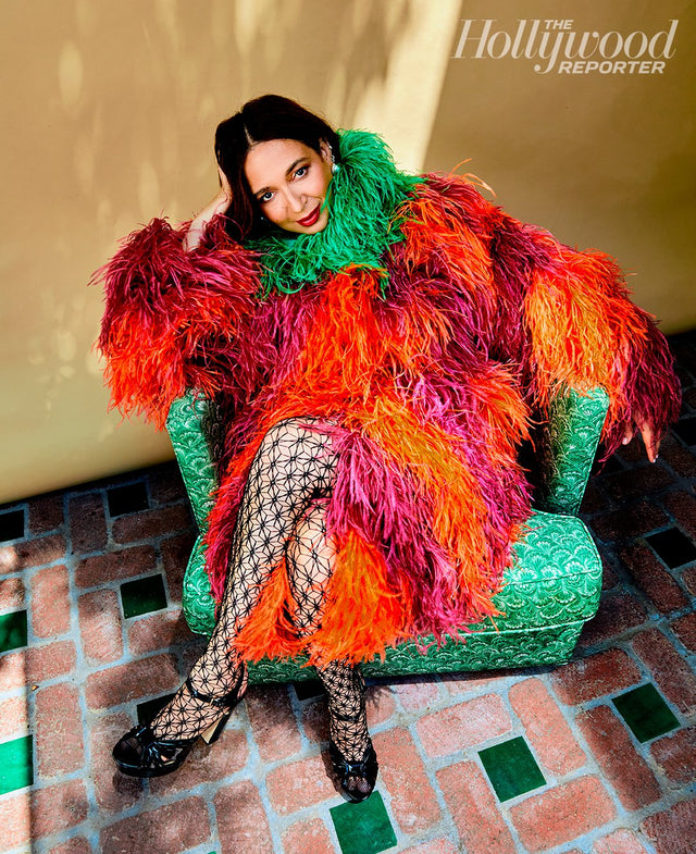 Woman in a colorful feathered coat seated on a green chair