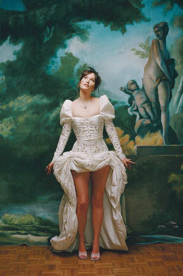 Woman in an ornate white dress before a forest mural