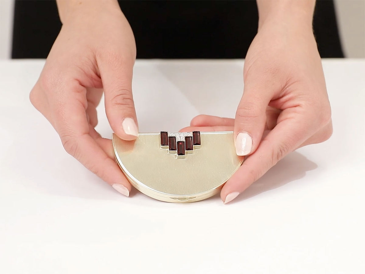 Half moon gold box with garnet and diamond accents held by hand