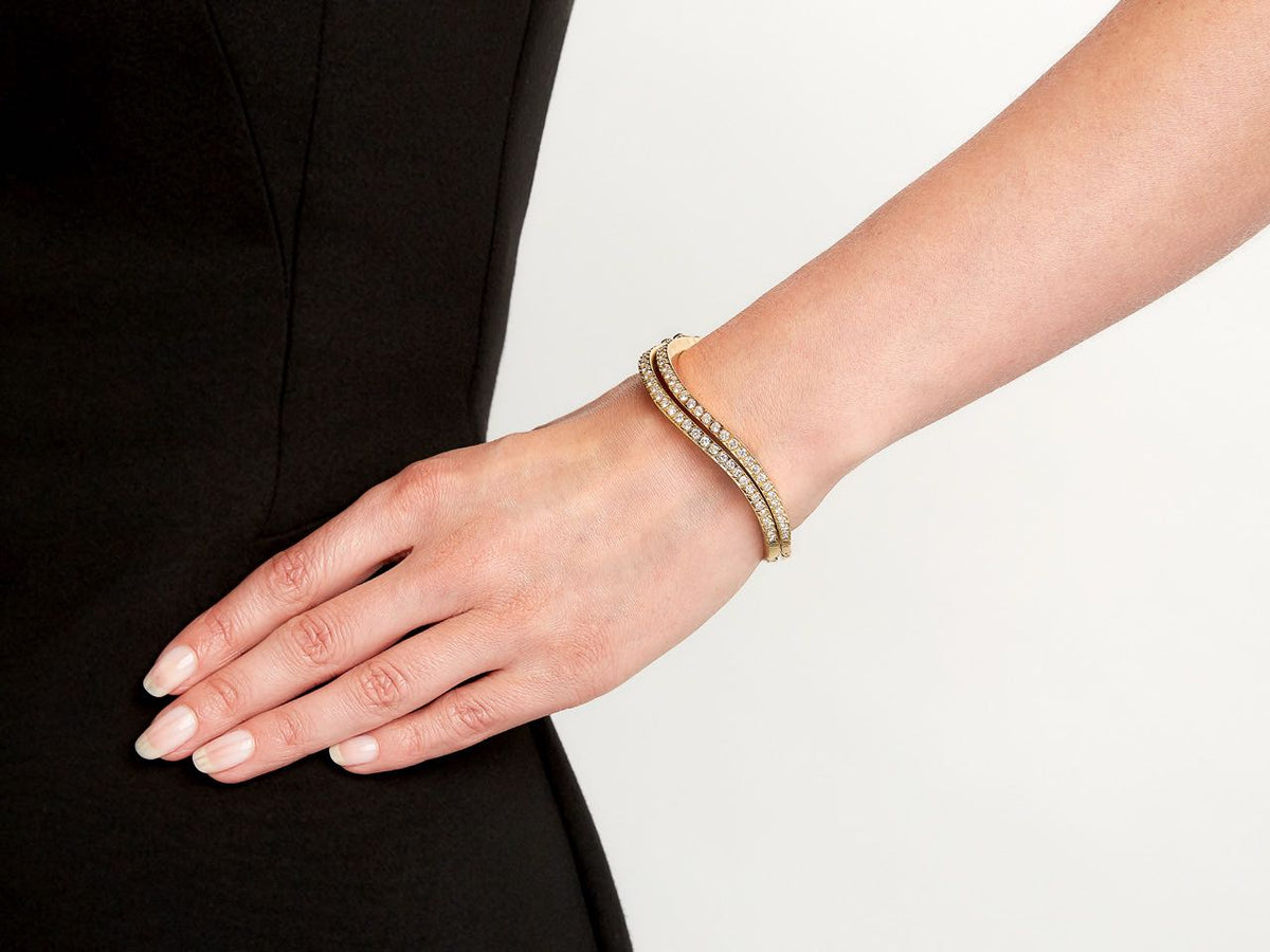 Wrist wearing two diamond wave bangles in gold
