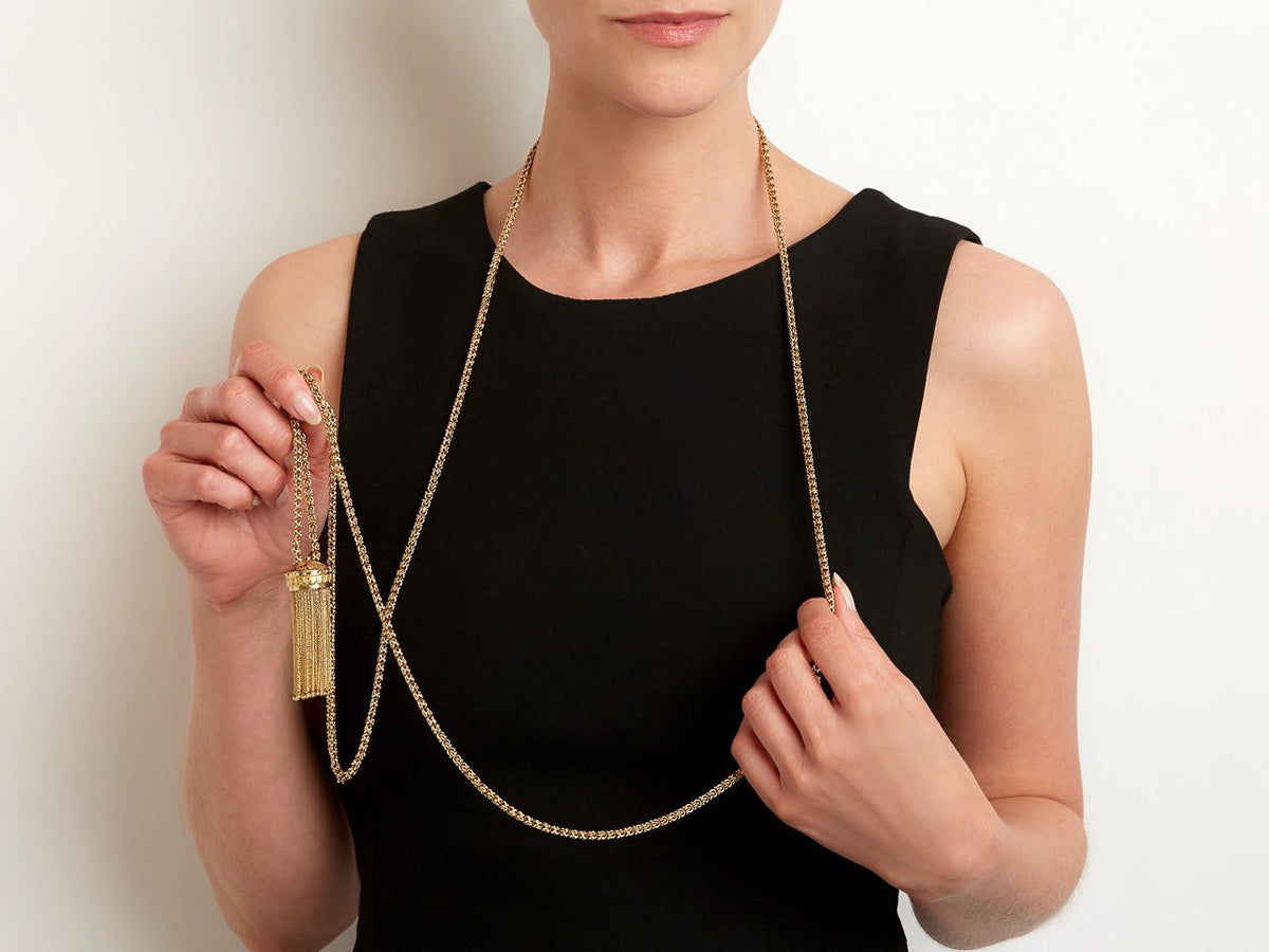 Model wearing a long gold tassel necklace with black enamel crown