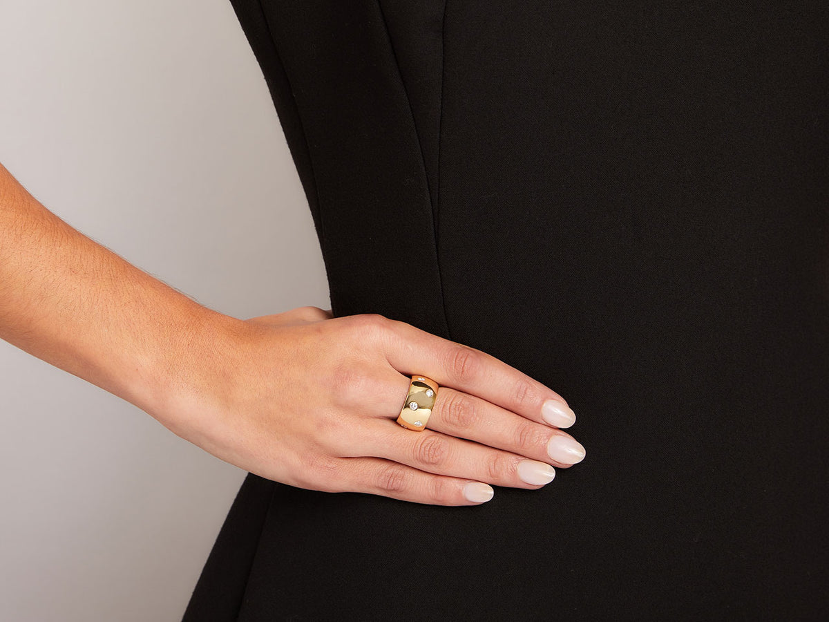 Hand wearing a wide 18k gold diamond band