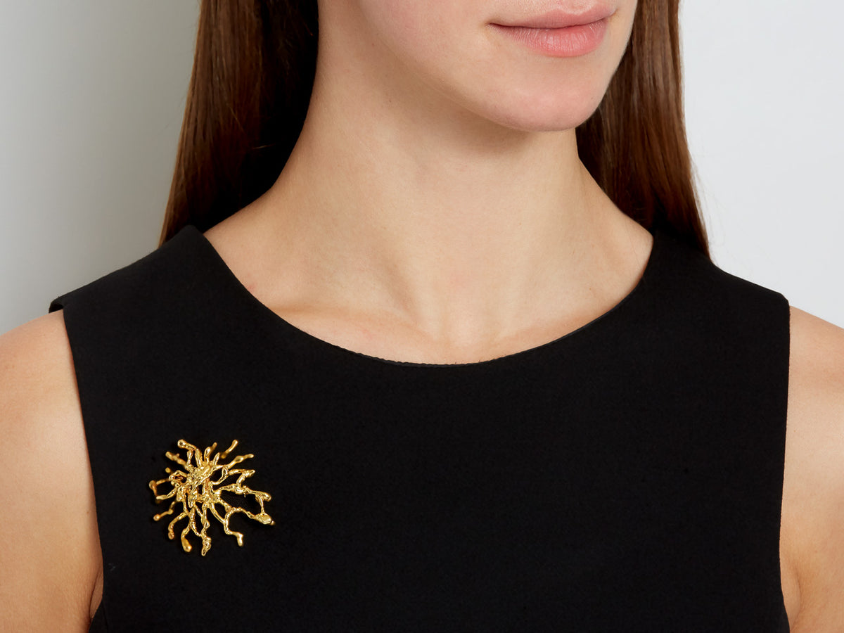 Asymmetrical textured 18K gold brooch on black dress