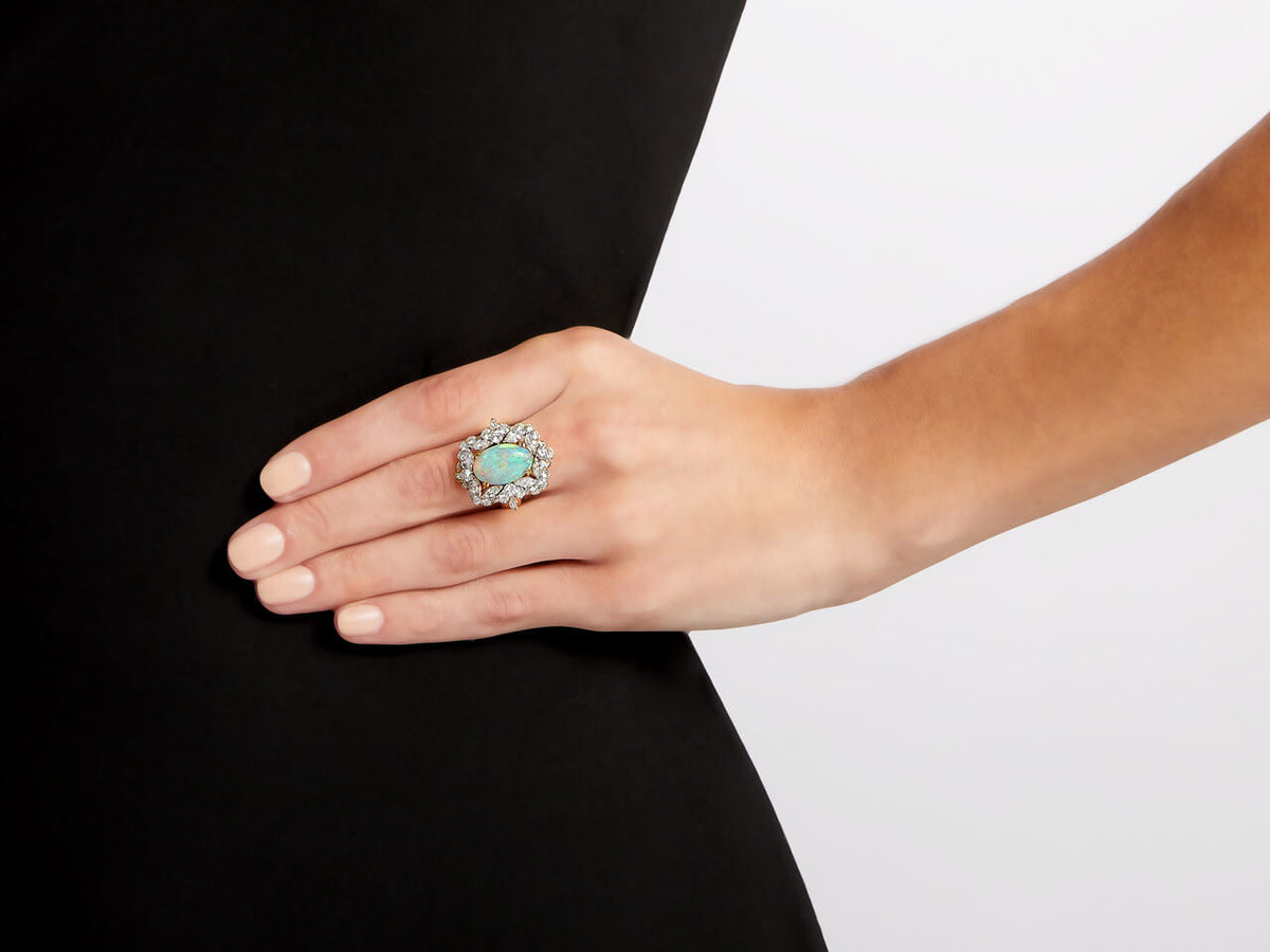 Hand wearing an oval white opal and diamond halo ring